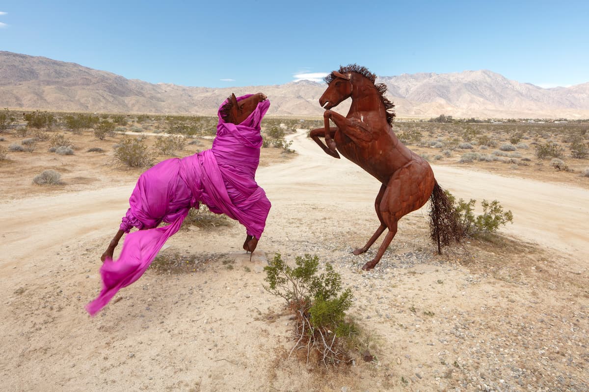 Two steel horse scultures in the desert facing off, one wrapped in pink cloth